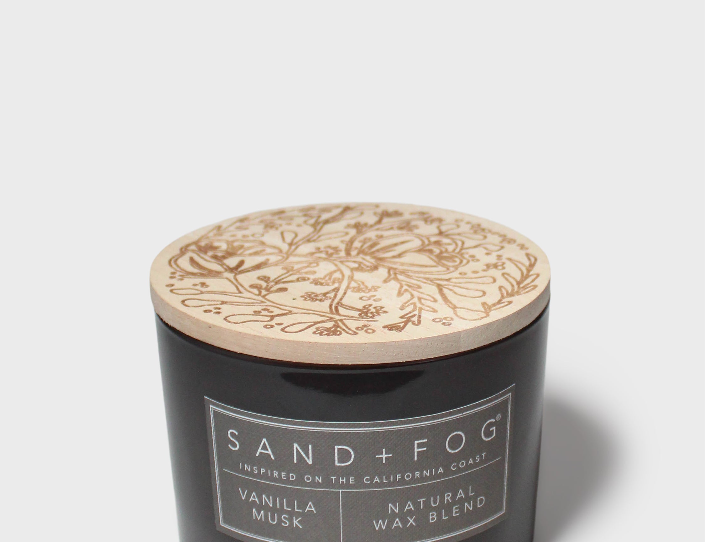 Scented candle in black glass jar with tan lid and Vanilla & Musk label