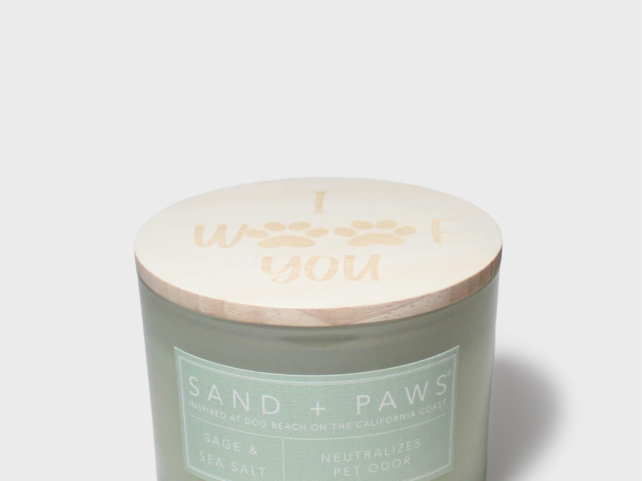 Sage green scented candle in glass jar with printed “Sand + Paws” label