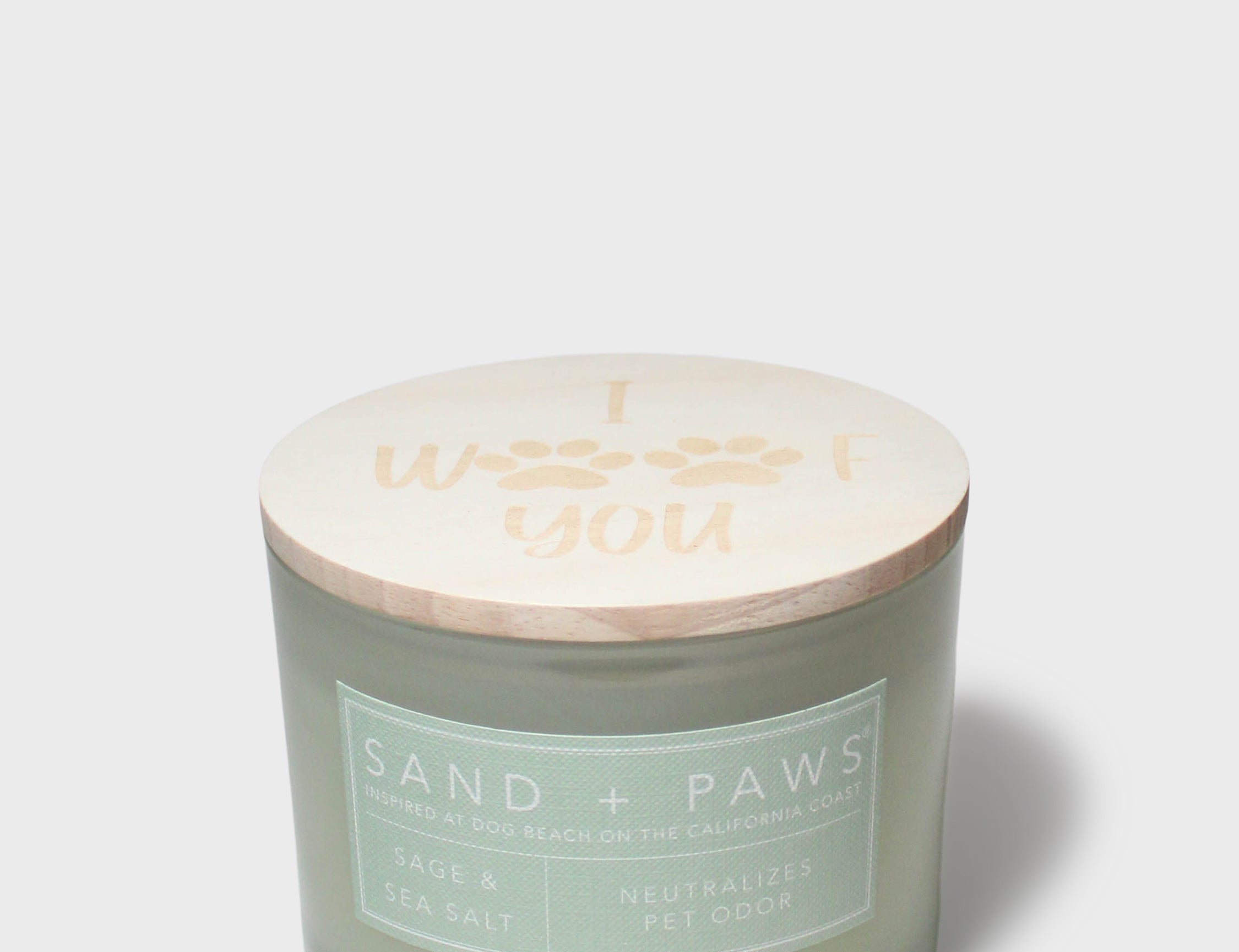 Sage green scented candle in glass jar with printed “Sand + Paws” label