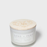 Scented candle with beige paw-print lid and Sand + Paws label