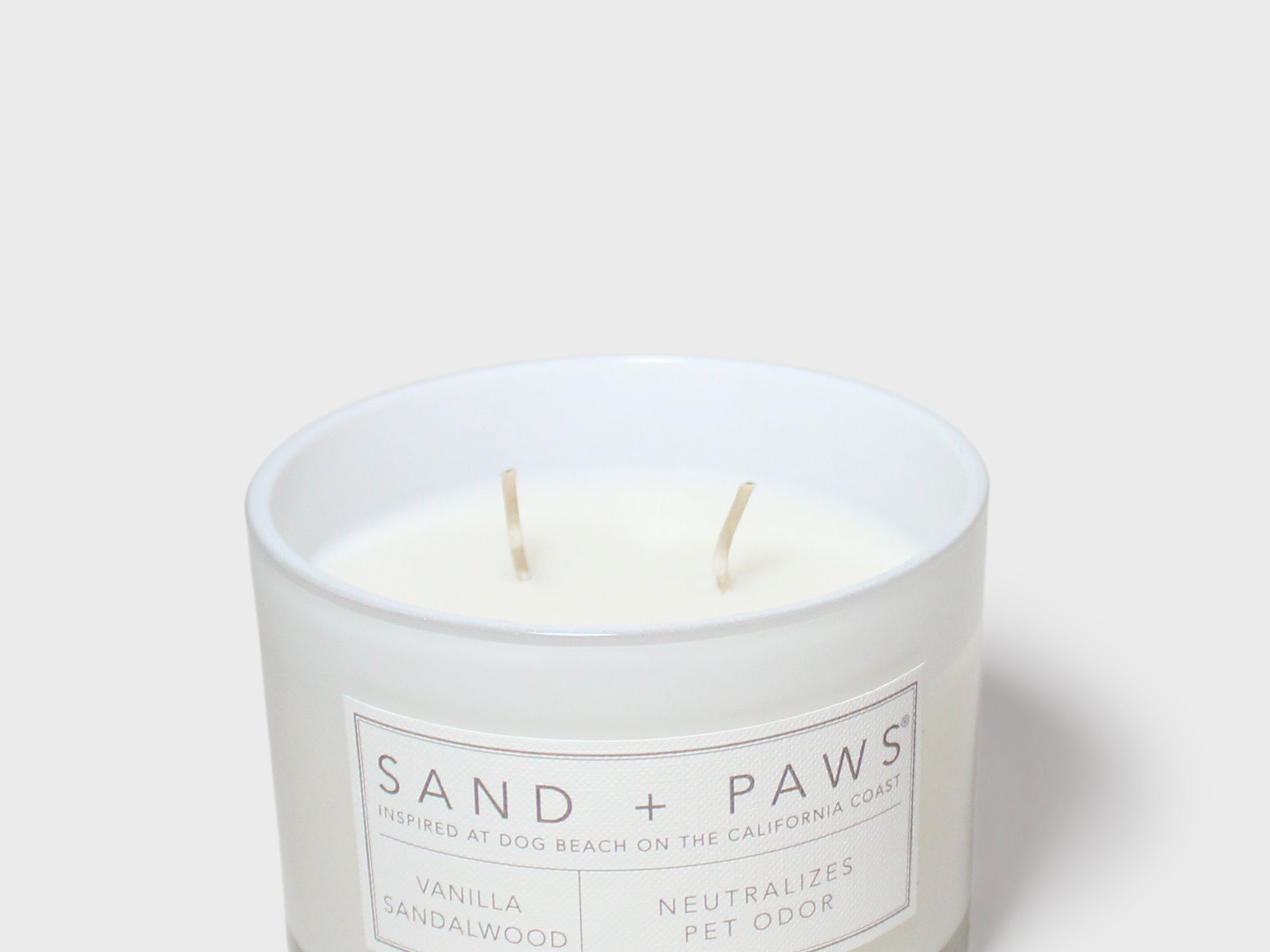 White scented candle jar with Sand + Paws label and two wicks