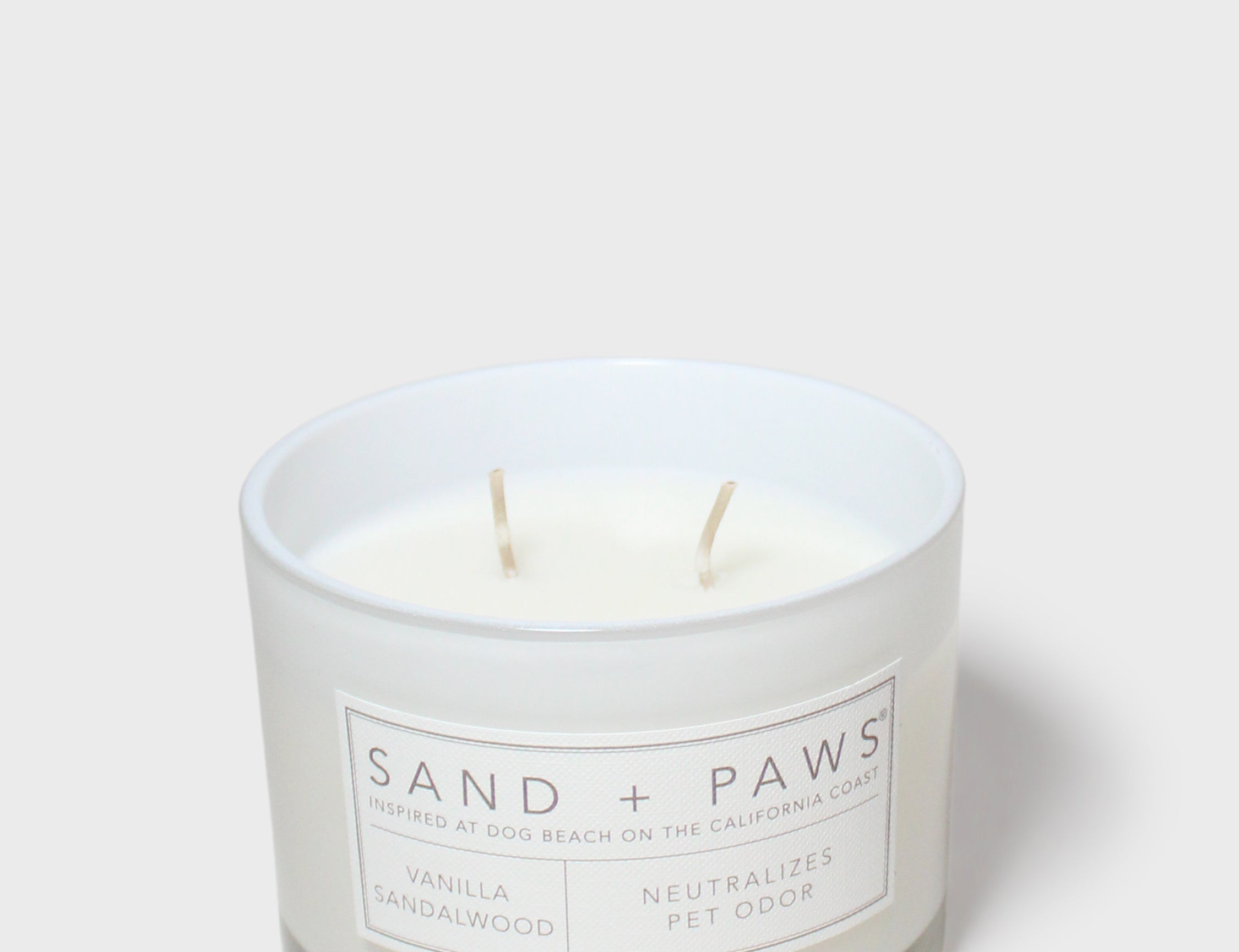 White scented candle jar with Sand + Paws label and two wicks