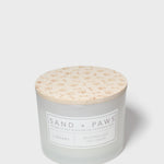 12 oz scented candle with Sand + Paws label and cream patterned lid top