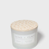 12 oz scented candle with Sand + Paws label and cream patterned lid top