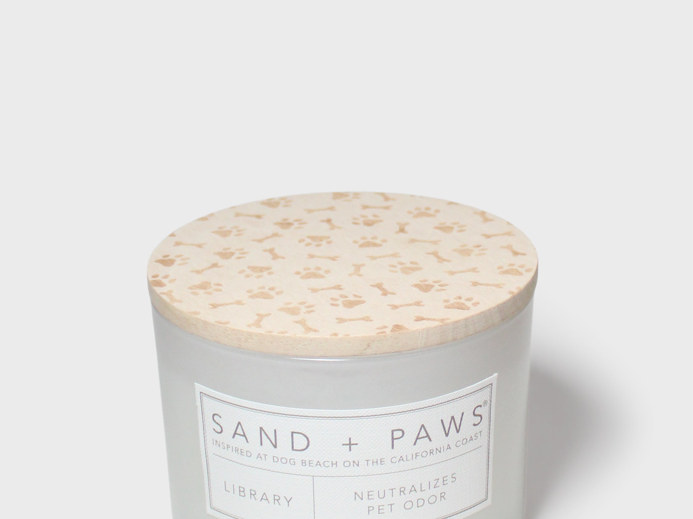 12 oz scented candle with Sand + Paws label and cream patterned lid top