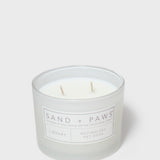 12 oz scented candle jar, Sand + Paws label, two wooden wicks visible