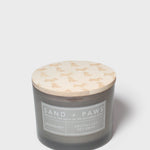 Gray glass jar scented candle with cream dog-pattern lid and 'Sand + Paws' label