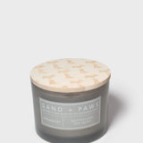 Gray glass jar scented candle with cream dog-pattern lid and 'Sand + Paws' label