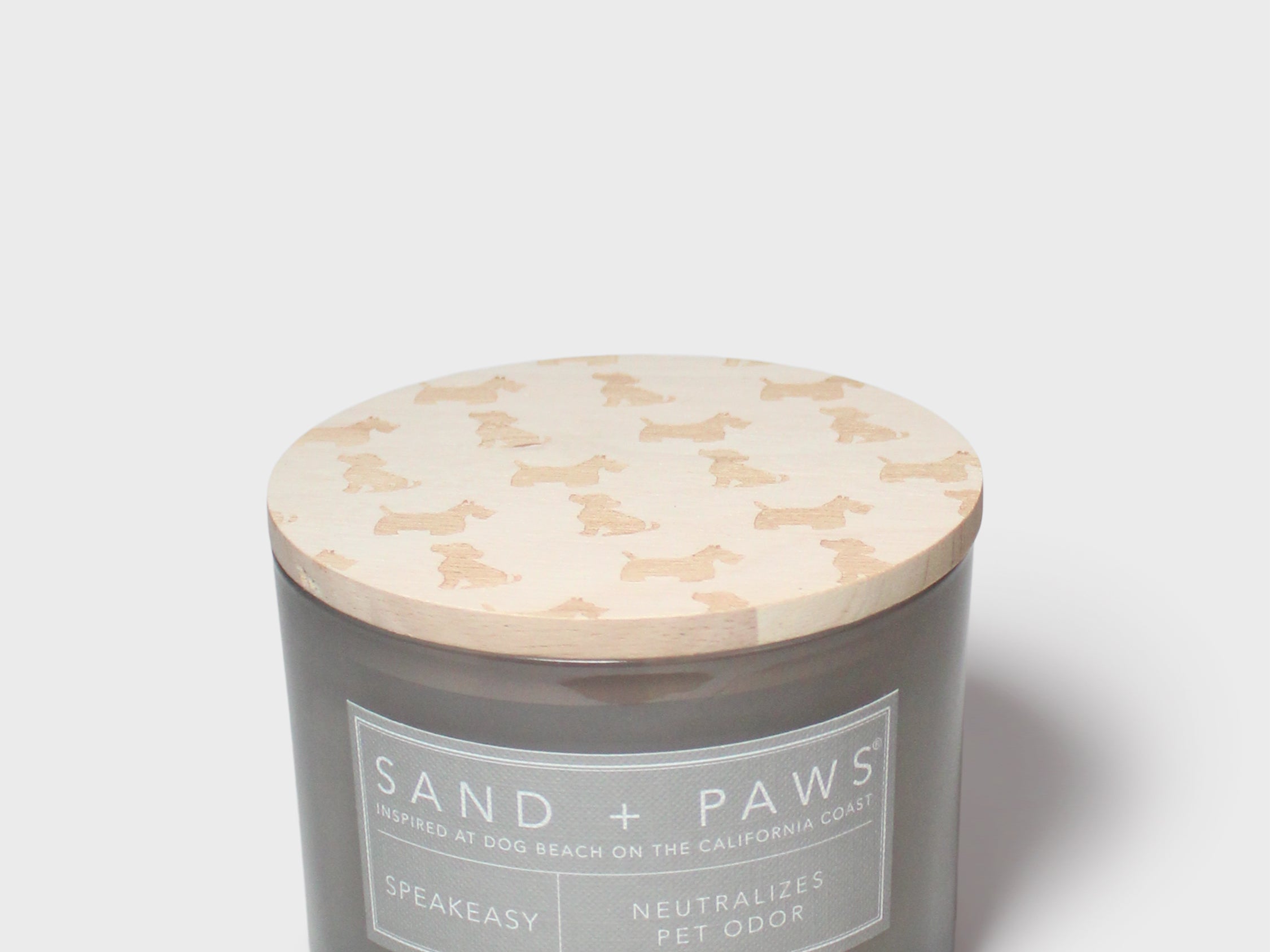 Gray glass jar scented candle with cream dog-pattern lid and 'Sand + Paws' label