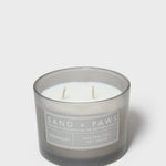 Gray glass jar scented candle with white wick and 'Sand + Paws' Speakeasy label