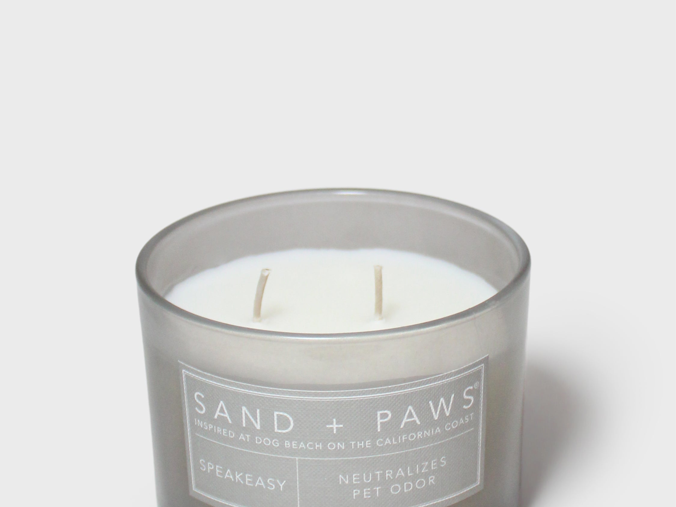Gray glass jar scented candle with white wick and 'Sand + Paws' Speakeasy label