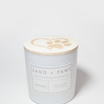 White candle jar with Sand + Paws Library label and lid paw-print top