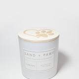 White candle jar with Sand + Paws Library label and lid paw-print top