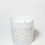 White candle jar with Sand + Paws Library label and neutralizes pet odor wording