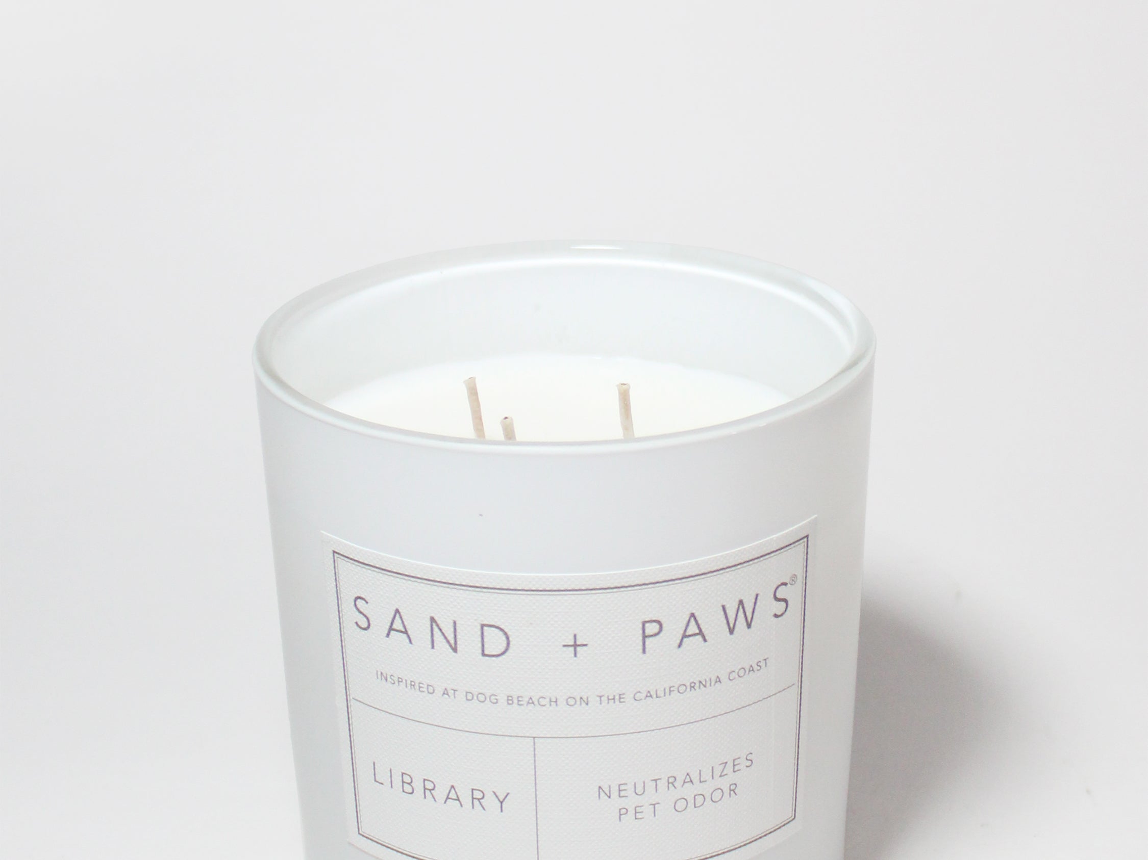 White candle jar with Sand + Paws Library label and neutralizes pet odor wording