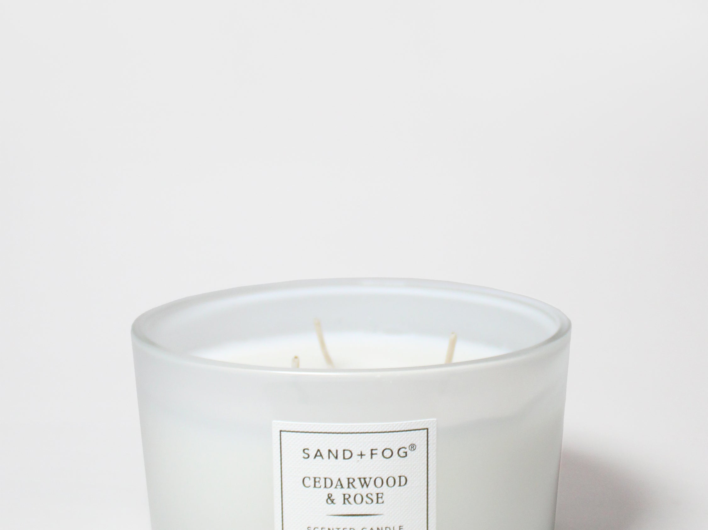 White scented candle in a glass jar with a centered Cedarwood & Rose label