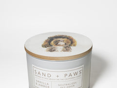 Scented candle jar with Sand + Paws label and dog artwork on the lid top