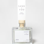 SAND + FOG Library reed diffuser in a clear glass bottle with a wooden cap.