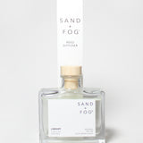 SAND + FOG Library reed diffuser in a clear glass bottle with a wooden cap.