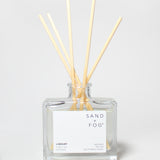 SAND + FOG Library reed diffuser with pale wooden reeds in a clear glass bottle.
