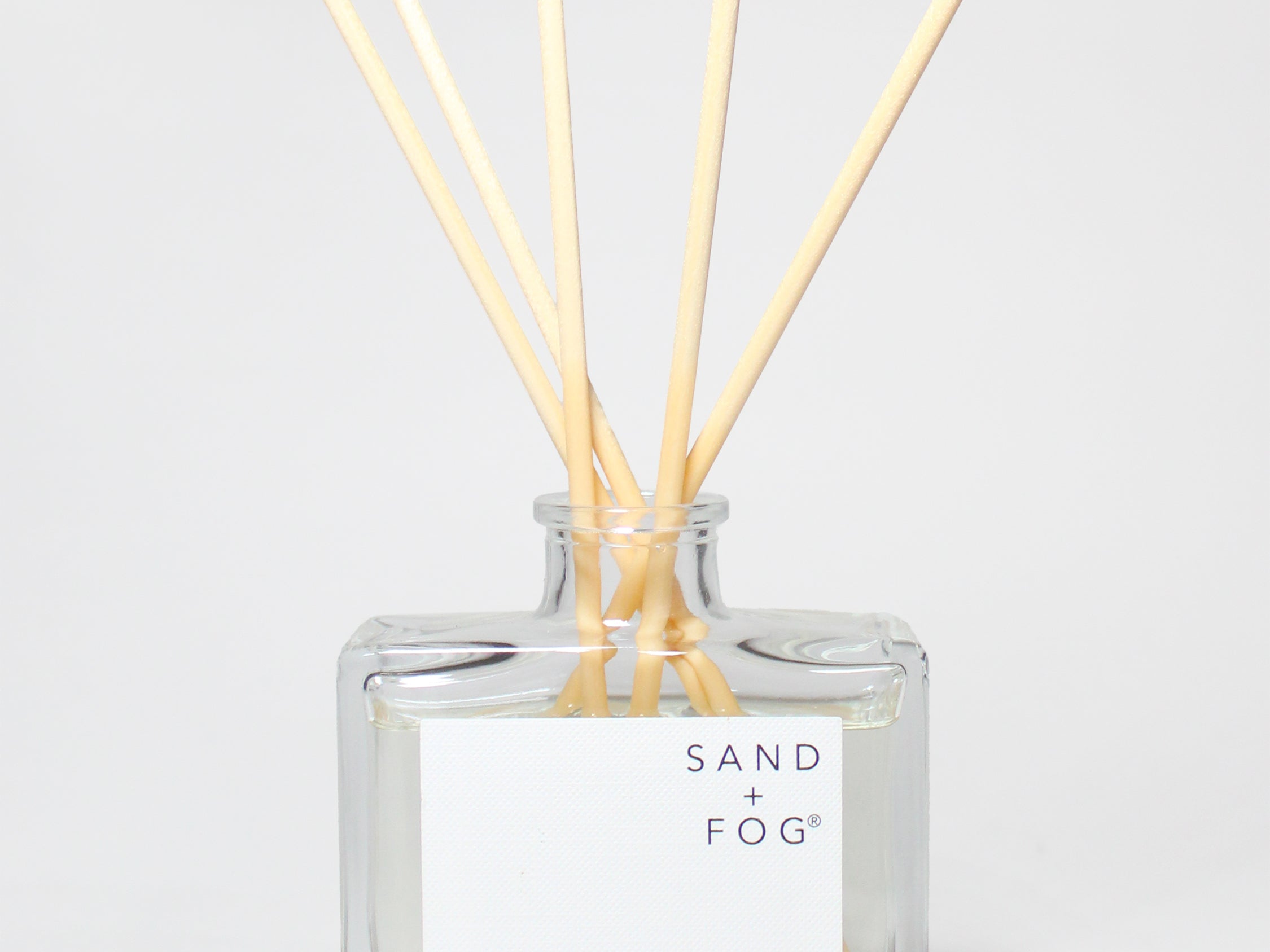 SAND + FOG Library reed diffuser with pale wooden reeds in a clear glass bottle.