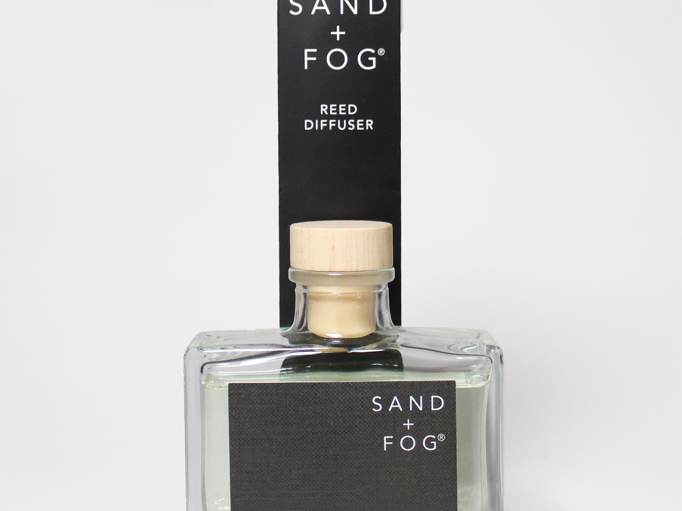 Teakwood reed diffuser in a clear glass bottle with a wood cap beside its black box.