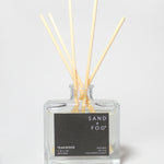 Teakwood reed diffuser in a clear glass bottle with wooden reeds and a black label.