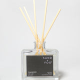 Teakwood reed diffuser in a clear glass bottle with wooden reeds and a black label.