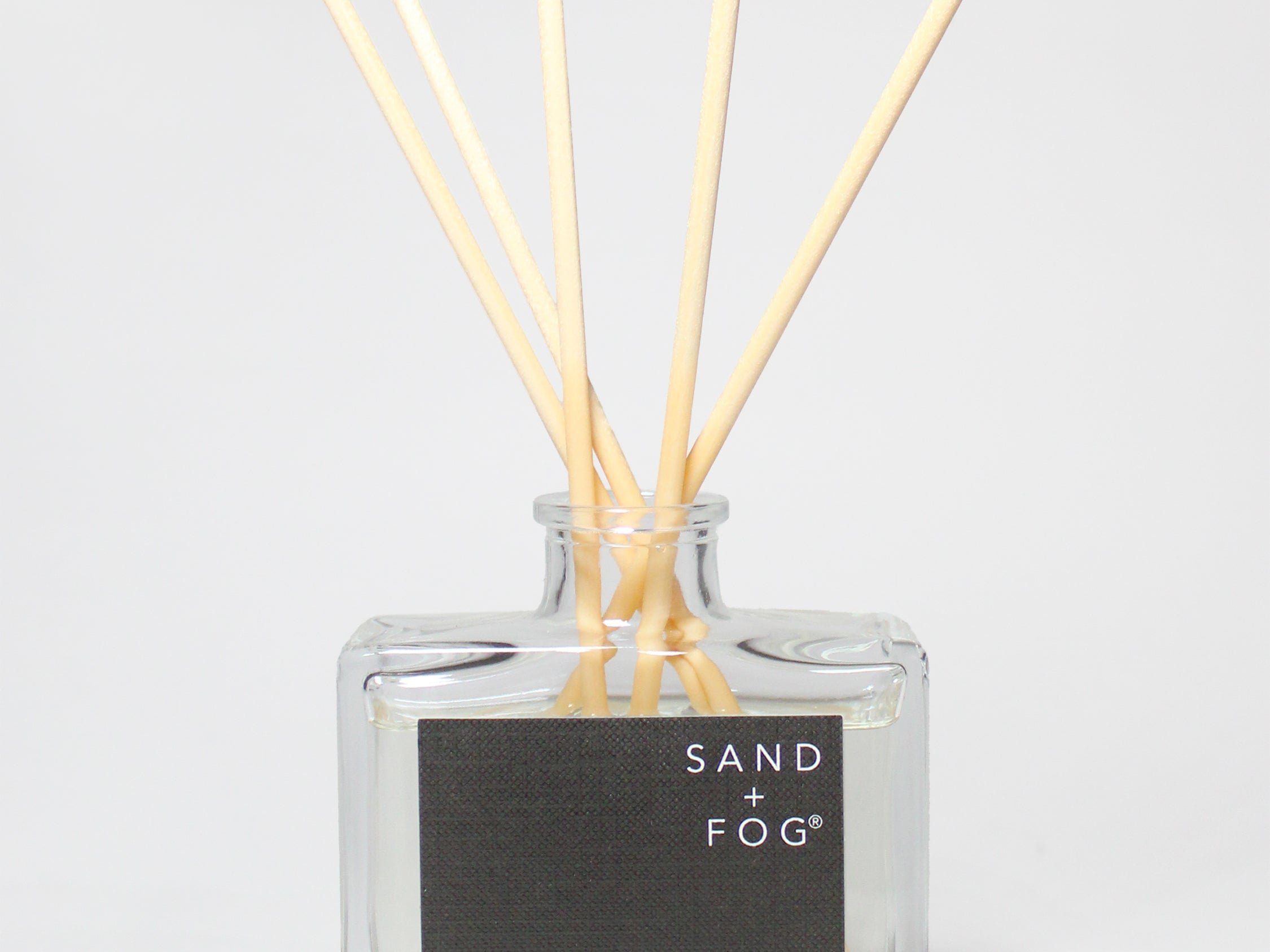 Teakwood reed diffuser in a clear glass bottle with wooden reeds and a black label.