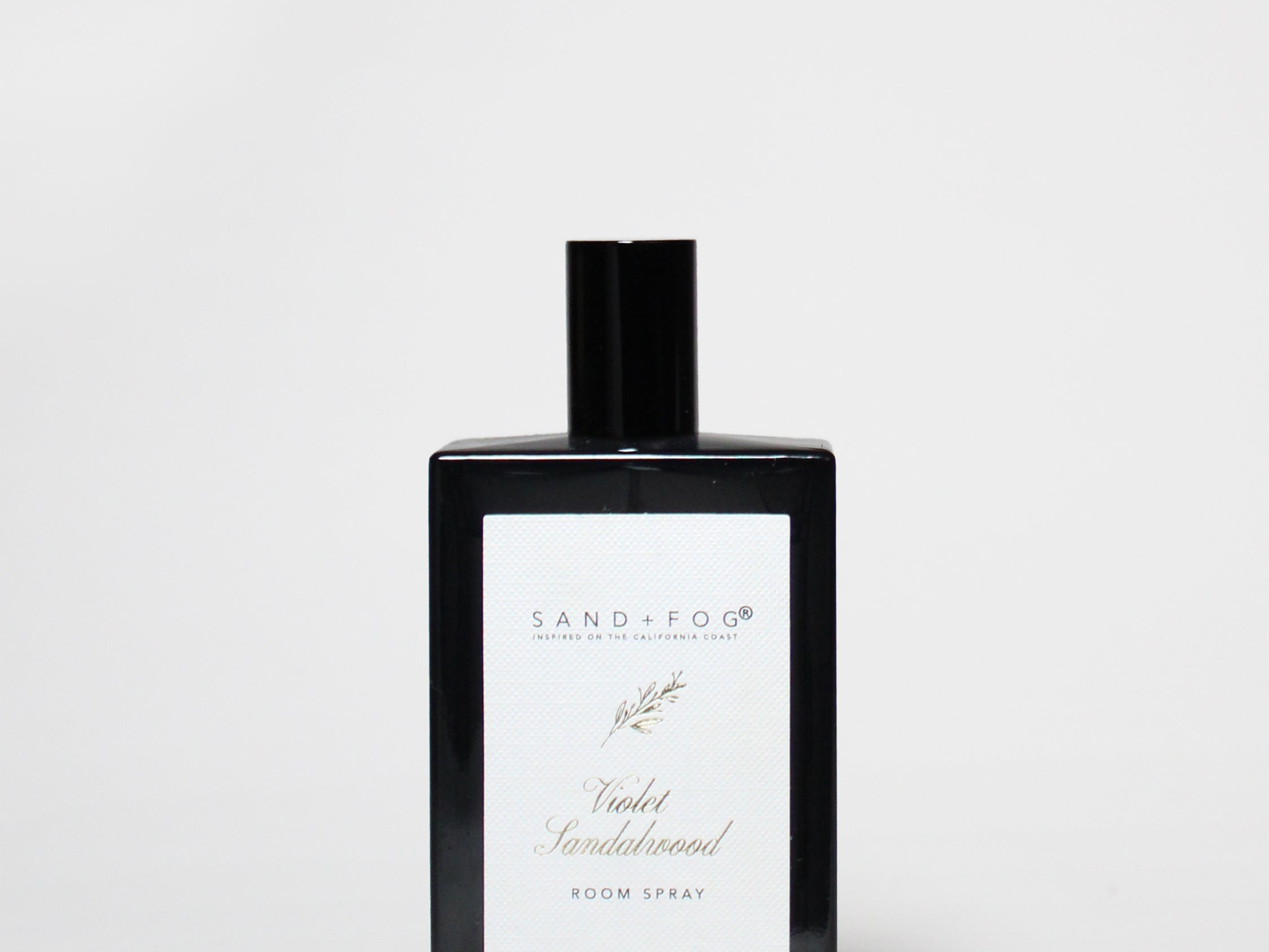 Room spray bottle with black cap and white label on dark glass