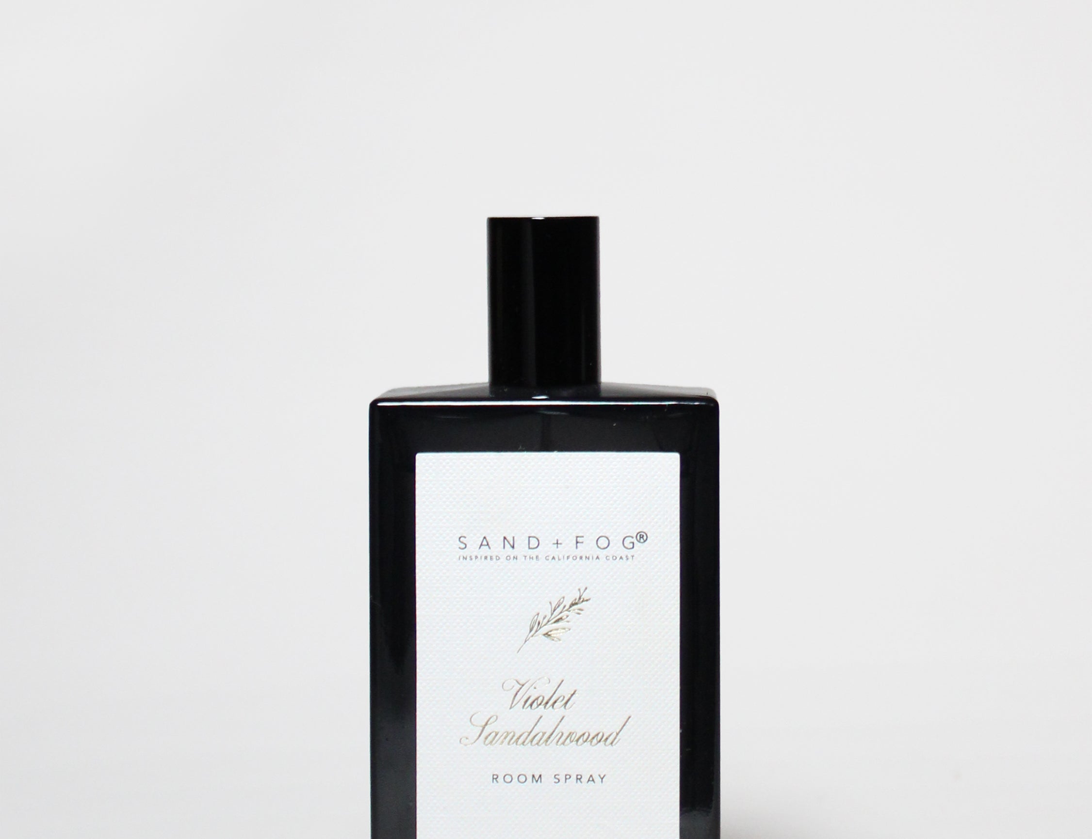 Room spray bottle with black cap and white label on dark glass