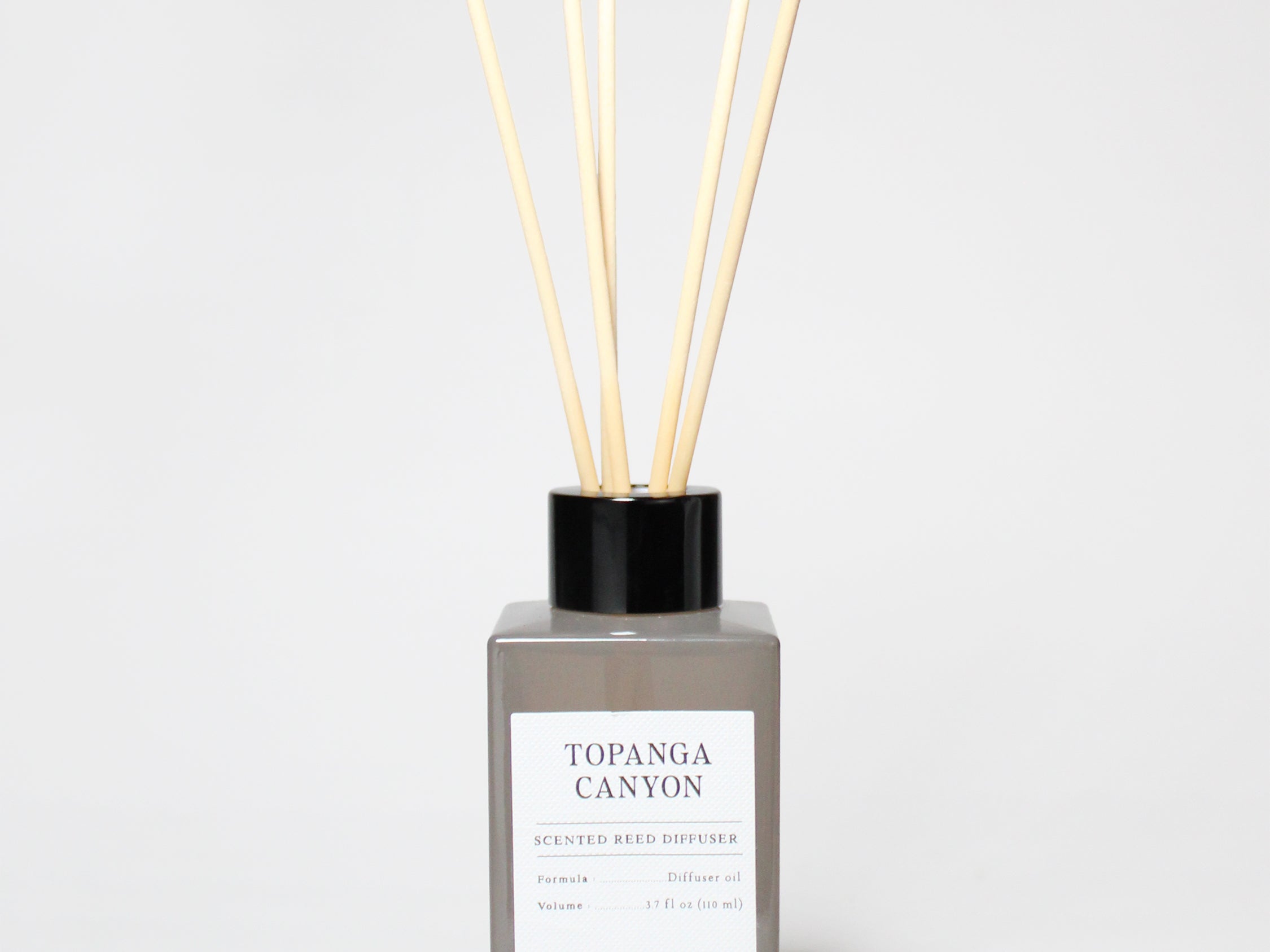 Topgana Canyon reed diffuser in a gray bottle with black cap and several reeds