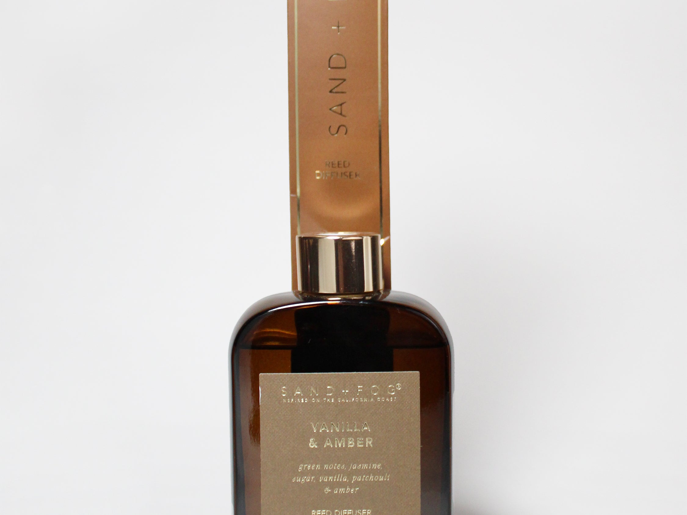 Vanilla and amber reed diffuser in an amber glass bottle with a tall gold-toned carton.