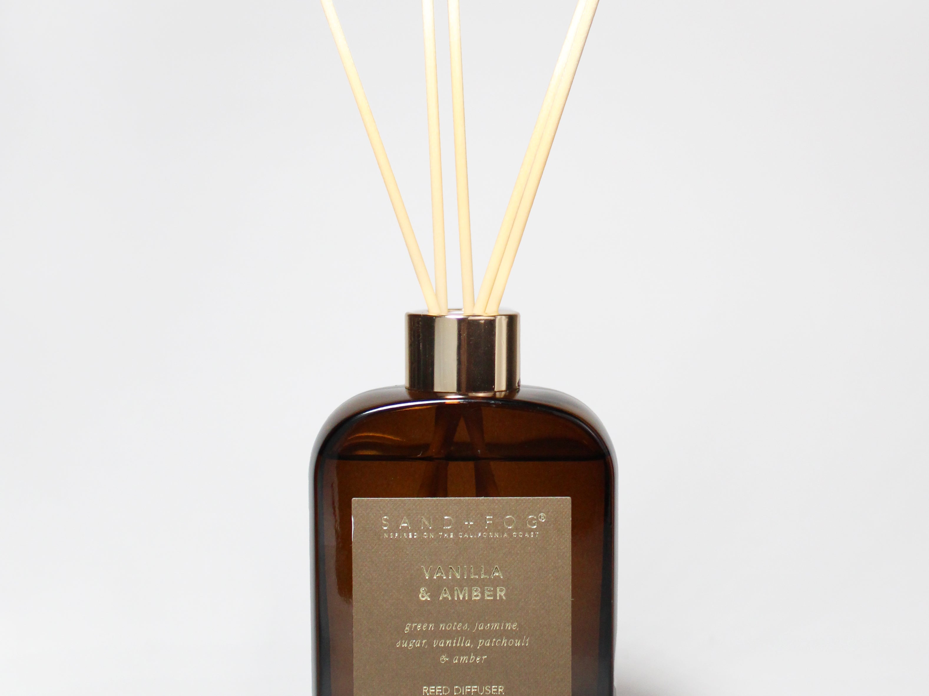 Vanilla and amber reed diffuser in a dark amber glass bottle with pale reeds.