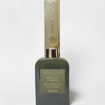Bergamot and neroli reed diffuser in a dark green glass bottle with a tall Sand + Fog box.