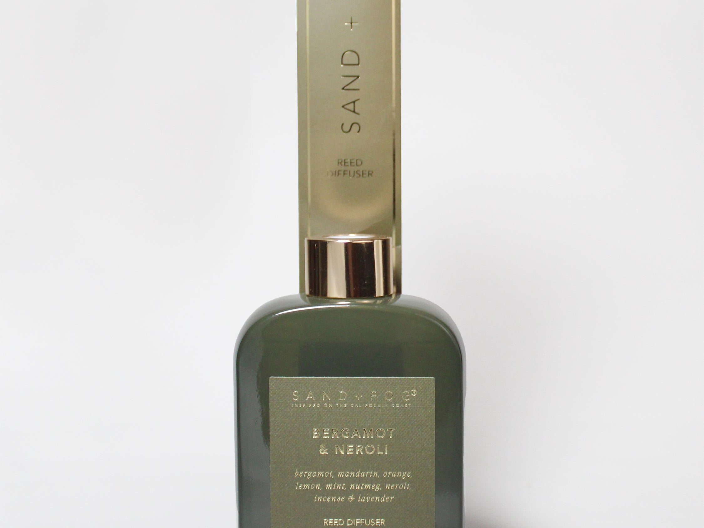 Bergamot and neroli reed diffuser in a dark green glass bottle with a tall Sand + Fog box.