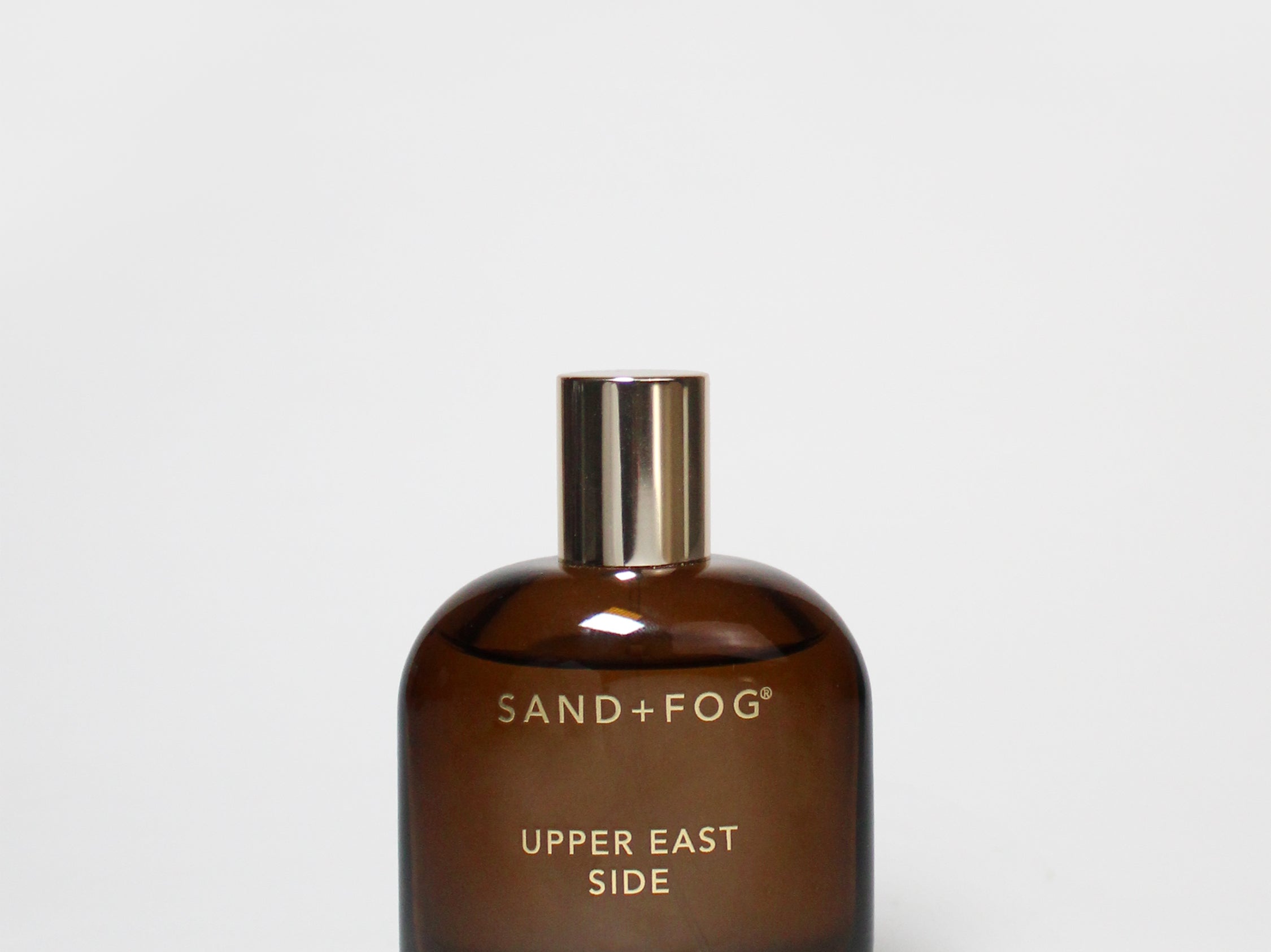 Amber glass room spray bottle with gold cap, labeled SAND+FOG UPPER EAST SIDE