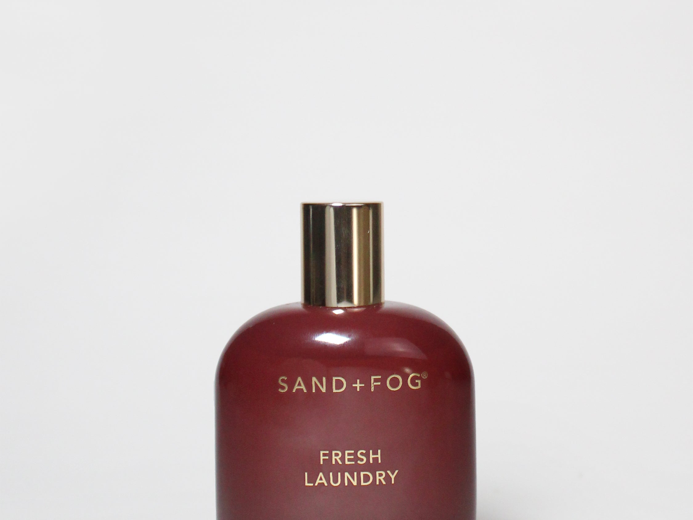Room spray bottle with dark red glass, gold cap, SAND+FOG Fresh Laundry label