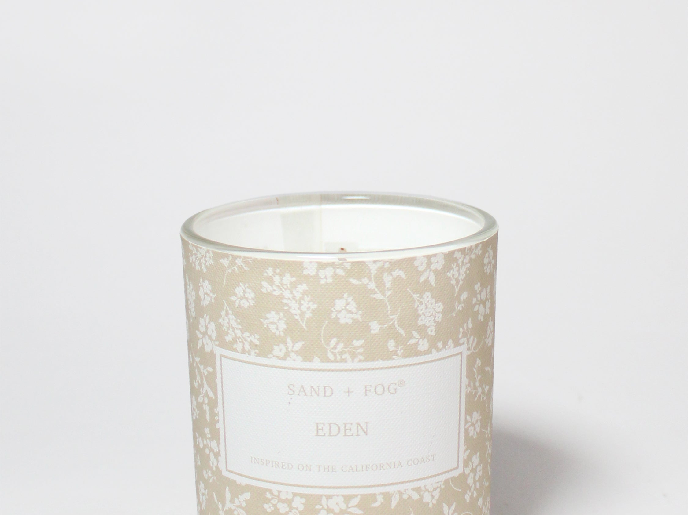 Eden 10 oz scented candle in a glass jar with a beige floral pattern and visible white wax.