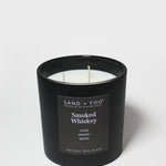 Black scented candle jar with two wicks and “Sand + Fog” Smoked Whiskey label