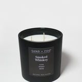 Black scented candle jar with two wicks and “Sand + Fog” Smoked Whiskey label