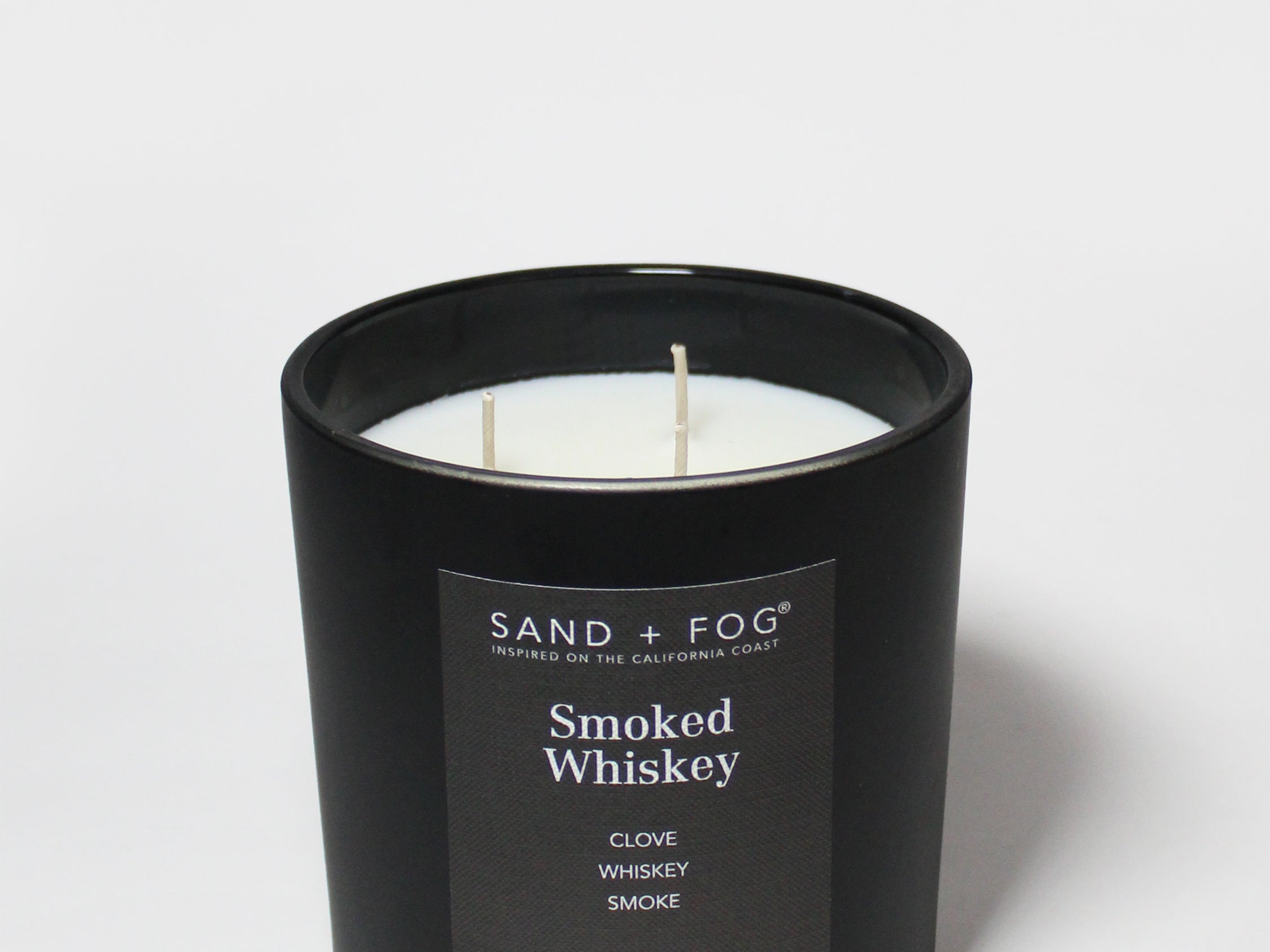 Black scented candle jar with two wicks and “Sand + Fog” Smoked Whiskey label