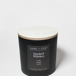 Black scented candle with lid and “Sand + Fog” Smoked Whiskey label, 21 oz jar