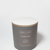 Teakwood scented candle in dark gray jar with off-white wax top and tan rim