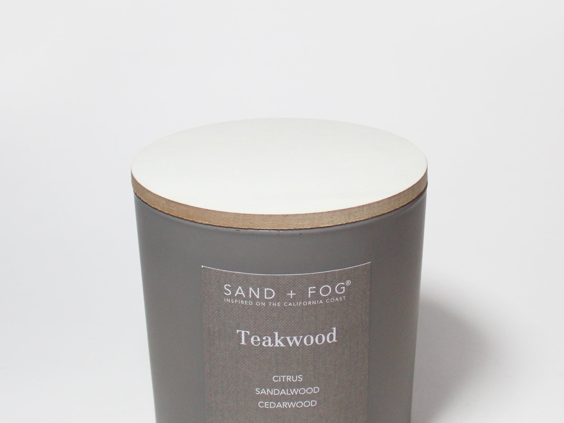 Teakwood scented candle in dark gray jar with off-white wax top and tan rim