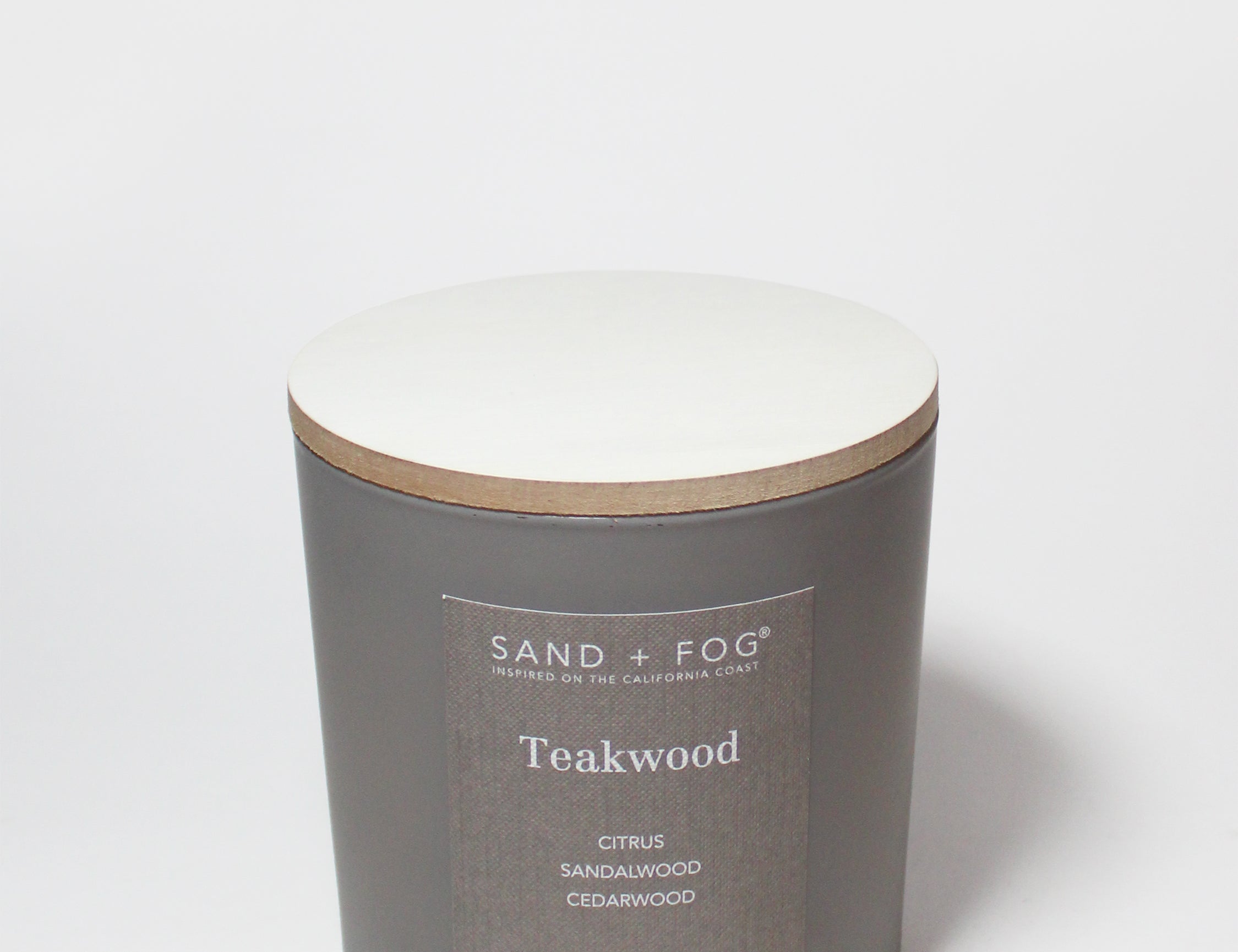 Teakwood scented candle in dark gray jar with off-white wax top and tan rim