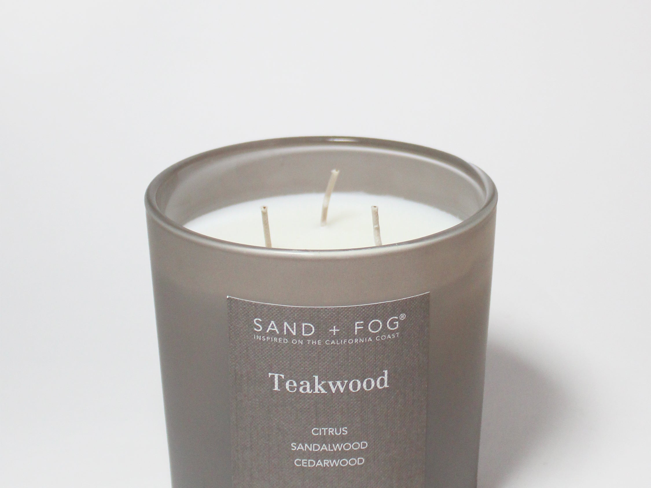 Teakwood scented candle in dark gray jar with three wicks and printed label