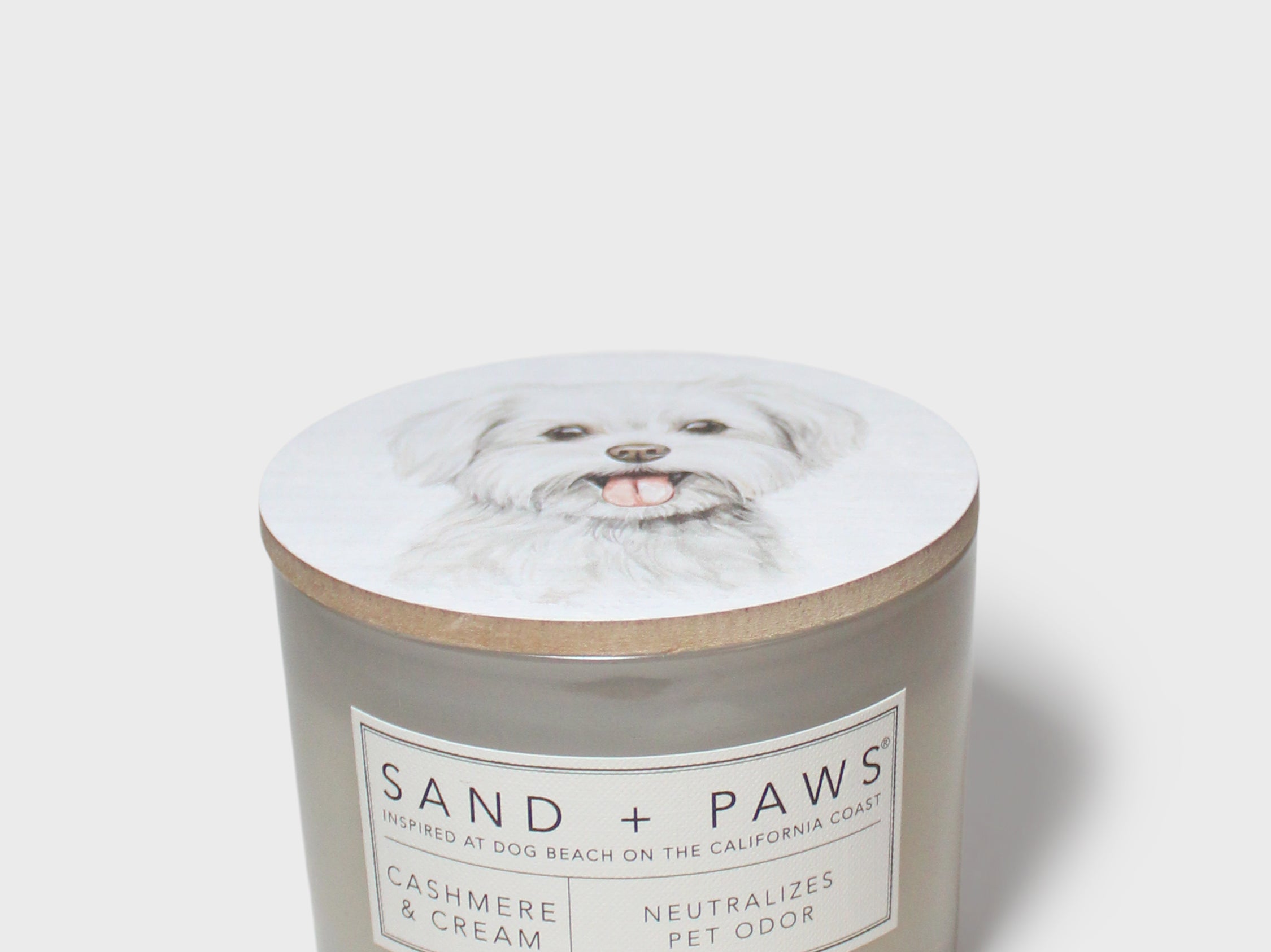 Sand + Paws scented candle jar with dog-portrait lid and cream 'SAND + PAWS' label