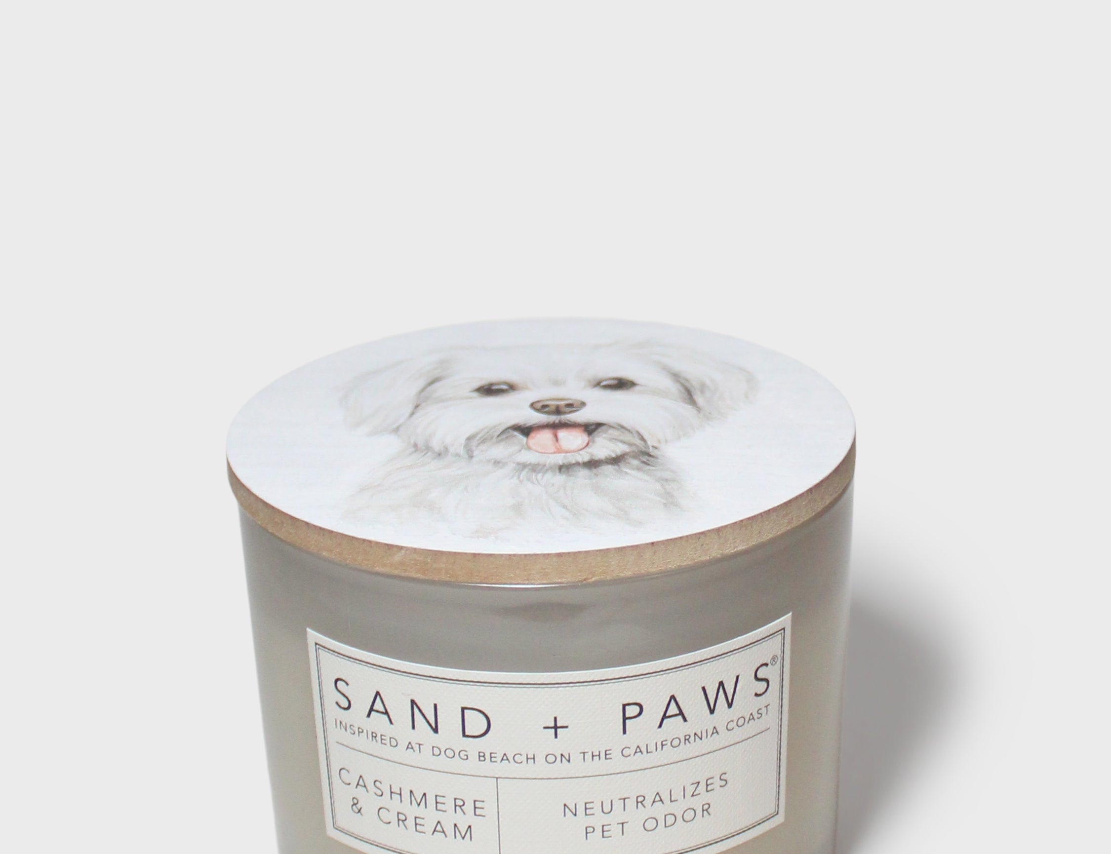 Sand + Paws scented candle jar with dog-portrait lid and cream 'SAND + PAWS' label