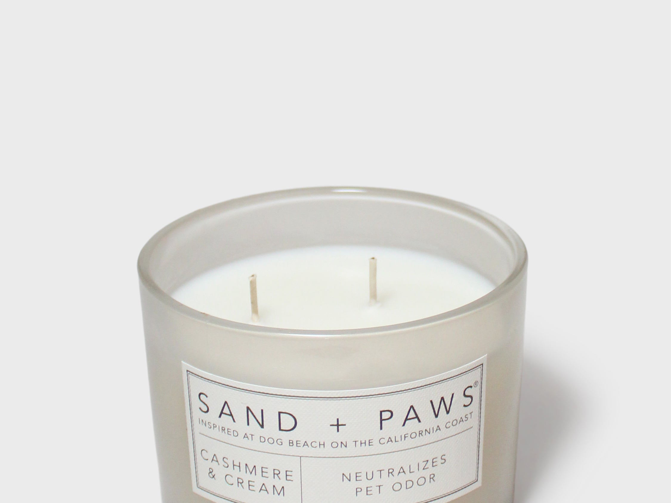 Sand + Paws scented candle jar with cream wax, two wicks, 'SAND + PAWS' label